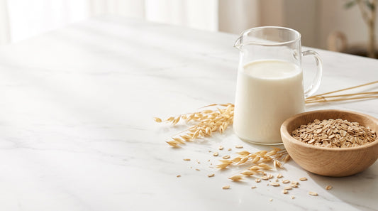 A glass jug of fresh goat milk and a bowl of rolled oats on a white marble counter