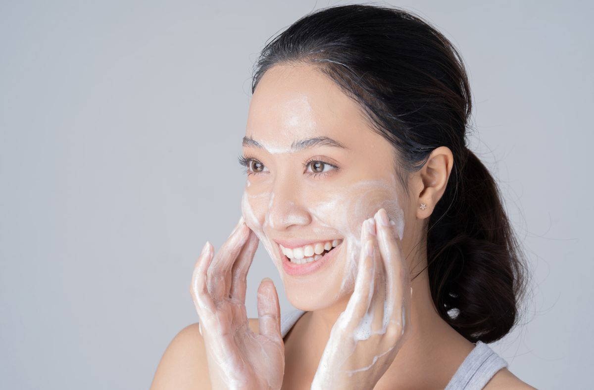 Woman applying cream to her face with a gray background