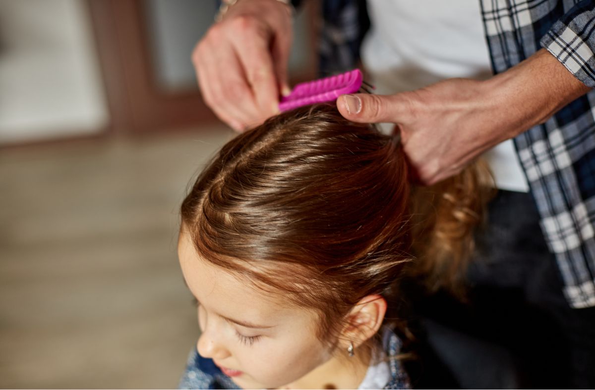 Person combing a child's hair with a pink comb in a home setting