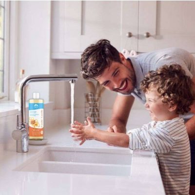 Man and child washing hands in a kitchen sink with a bottle of soap on the counter.