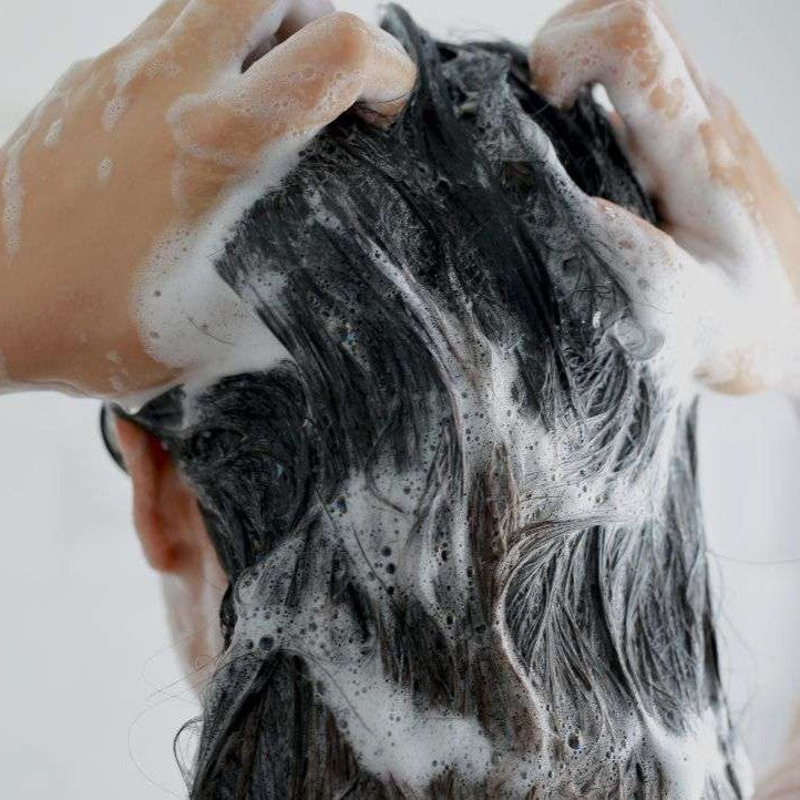 Person washing hair with soapy hands and a white background